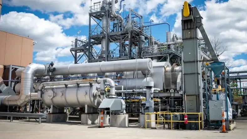Industrial processing plant with insulated steel pipework, large reactors, and yellow safety railings