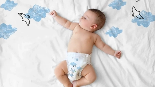 Infant in a patterned diaper lying on white fabric surrounded by hand-drawn cloud and bird illustrations