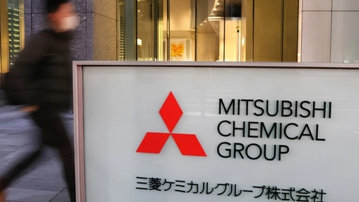 Mitsubishi Chemical Group entrance sign with Japanese text, a pedestrian blurred in motion passing behind