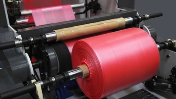 Red plastic film rolls on a rolling machine with mechanical components in a manufacturing environment