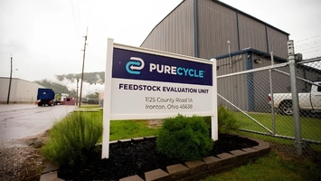 PureCycle site sign for its Feedstock Evaluation Unit with an industrial building and steam in the background