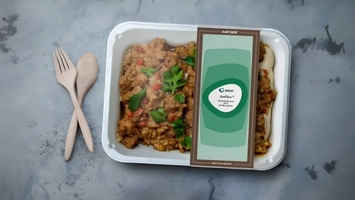 AmFiber fiber food tray with a chilled ready meal and green branded label beside wooden fork and spoon