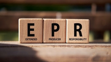 Wooden cubes spelling EPR for Extended Producer Responsibility on a wood surface with a green background